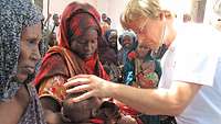 Ein Arzt untersucht ein afrikanisches Kind auf dem Arm der Mutter