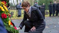 Ministerin Kramp-Karrenbauer kniet vor einem Gedenkkranz.