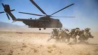 Soldaten hocken vor einem startenden Transporthubschrauber vom Typ CH-53