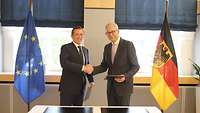 Gerd Hoofe und Lionel Souque geben sich die Hand und schauen in die Kamera