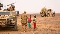 Soldaten im Gespräch mit einheimischen Kindern, daneben Bundeswehrfahrzeuge