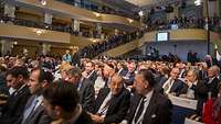 Menschen sotzen in einem großen Saal.
