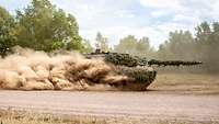 Ein Panzer fährt durch ein Gelände und wirbelt Staub auf