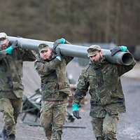 Vier Soldaten tragen ein Rohr