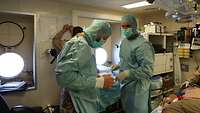 Soldaten ziehen OP-Kleidung an, im Hintergrund schreibt Soldat Patientendaten auf