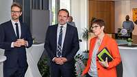 Kramp-Karrenbauer steht neben zwei männlichen Personen in einen Raum