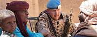 Ein deutscher Soldat mit blauem Barett sitzt mit afrikanischen Männern zusammen und spricht mit ihnen