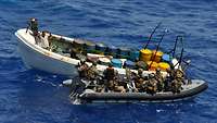 Ein Motorboot mit mehreren Soldaten und ein vermutliches Piraten-Boot auf dem Meer