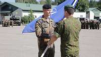 Ein litauischer Soldat übergibt einem deutschen Soldaten die NATO-Flagge