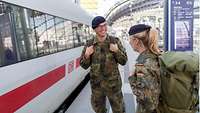Eine Soldatin und ein Soldat stehen neben einem Zug auf einem Bahnsteig