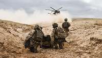 Soldaten in staubiger Landschaft, im Hintergrund ein Hubschrauber