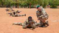 Ein Bundeswehrsoldat kniet neben malischen Soldaten, die mit Waffen auf dem Boden liegen