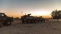 Drei gepanzerte Militärfahrzeuge fahren hintereinander bei Dämmerung