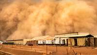 Eine Sandwolke rollt über ein Camp aus flachen Häusern und Containern