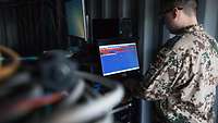 Ein Soldat arbeitet stehend an einem Computer in einem Serverraum