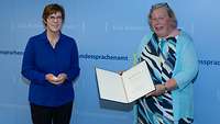 Ministerin Kramp-Karrenbauer steht neben einer Frau vor einer blauen Wand mit der Aufschrift „Bundessprachenamt“