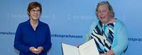 Ministerin Kramp-Karrenbauer steht neben einer Frau vor einer blauen Wand mit der Aufschrift „Bundessprachenamt“
