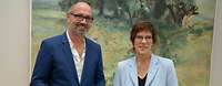 Ministerin Kramp-Karrenbauer und eine männliche Person, die ein Dokument in der Hand hält, stehen lächelnd nebeneinander
