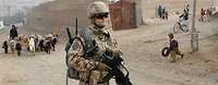 Ein Soldat in Afghanistan mit einem Gewehr in der Hand. Im Hintergrund afghanische Kinder und ein Hirte mit Esel und Schafen. 