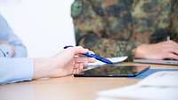 Die Hand einer Soldatin hält einem Stift über ein Tablet, das auf einem Tisch liegt