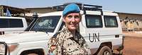 A Portrait of a smiling soldier wearing a blue beret in front an UN vehicle