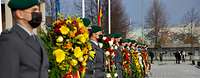 Mehrere Soldatinnen und Soldaten im Dienstanzug stehen in einer Reihe, zwischen ihnen Blumengestecke. 