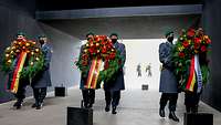 Sechs Soldaten im Dienstanzug tragen große Blumenkränze zum Ehrenmal.
