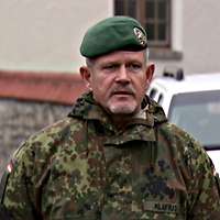 Ein Soldat steht mit verschänkten Armen hinter dem Rücken vor einem weißen Vereinte Nationen-Auto. 