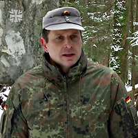 Ein Stabsoffizier steht in einem schneebedecktem Waldstück.