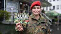 Eine Soldatin hält eine Postkarte mit der Aufschrift „Dein Jahr für Deutschland“ in die Kamera.