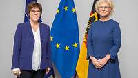 Kramp-Karrenbauer und Lambrecht stehen vor drei Fahnen