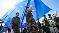 Several soldiers from different nations hoisting a large EU flag during a ceremony