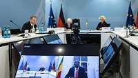 Ministerin Lambrecht sitzt mit weiteren Personen an einem Konferenztisch vor mehreren Bildschirmen und einer Kamera.