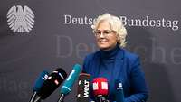 Ministerin Lambrecht spricht in die Mikrofone von Pressevertretern. Im Hintergrund das Logo des Deutschen Bundestages.