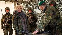 Ein Soldat spricht mit Ministerin Lambecht und zeigt ihr Ausrüstungsgegenstände.