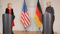 Ministerin Lambrecht und Amy Gutmann stehen an Rednerpulten. Hinter ihnen stehen die Flaggen von Deutschland und den USA.