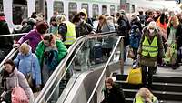 Viele Menschen mit Gepäck bewegen sich auf einem Bahnsteig.