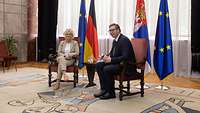 Ministerin Christine Lambrecht und der serbische Präsident Aleksandar Vučić sitzen vor Flaggen in einem Raum.