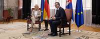 Ministerin Christine Lambrecht und der serbische Präsident Aleksandar Vučić sitzen vor Flaggen in einem Raum.