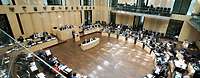 Mehrere Menschen sitzen in einem Saal während einer Versammlung, von oben fotografiert. 