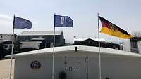 Die NATO-, KFOR- und Bundesdienstflagge sind nebeneinander an Stangen gehisst