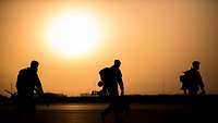 Drei Soldaten laufen beim Sonnenuntergang auf einem Flugplatz.