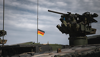 A weapon station with a heavy machine gun, the German flag flies in the background.