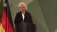 Christine Lambrecht steht am Rednerpult und spricht. Im Hintergrund rechts ist die Flagge der Bundesrepublik Deutschland.