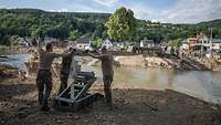 Three servicemen are helping to install a bridge section across a collapsed bridge 