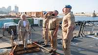 gerade tritt Ministerin Lambrecht an Bord eines Militärschiffes, begrüßt von drei Soldaten, im Hintergrund ein Containerhafen