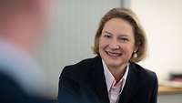 Frau Staffa schaut zu ihrem Gesprächspartner, der unscharf zu erkennen ist, sie lächelt offen.