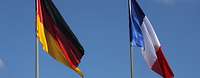 Eine deutsche und französische Flagge hängen vor blauem Himmel.