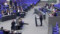 Parlamentssaal mit blauen Sitzen von der Seite, ein Mann am Rednerpult