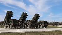 Drei LKW mit Raketen stehen auf einer Betonfläche. 